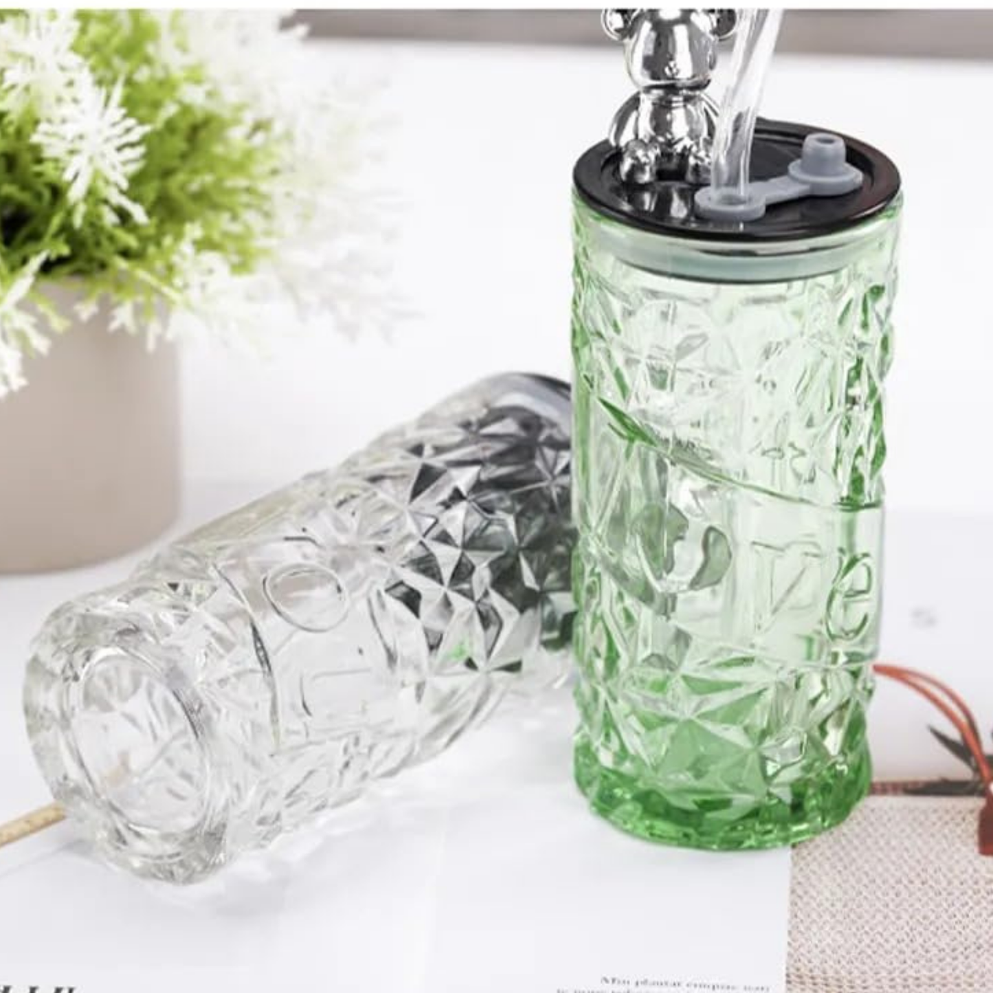 Green glass bottle with silver cap on a white surface with a plant in the background
