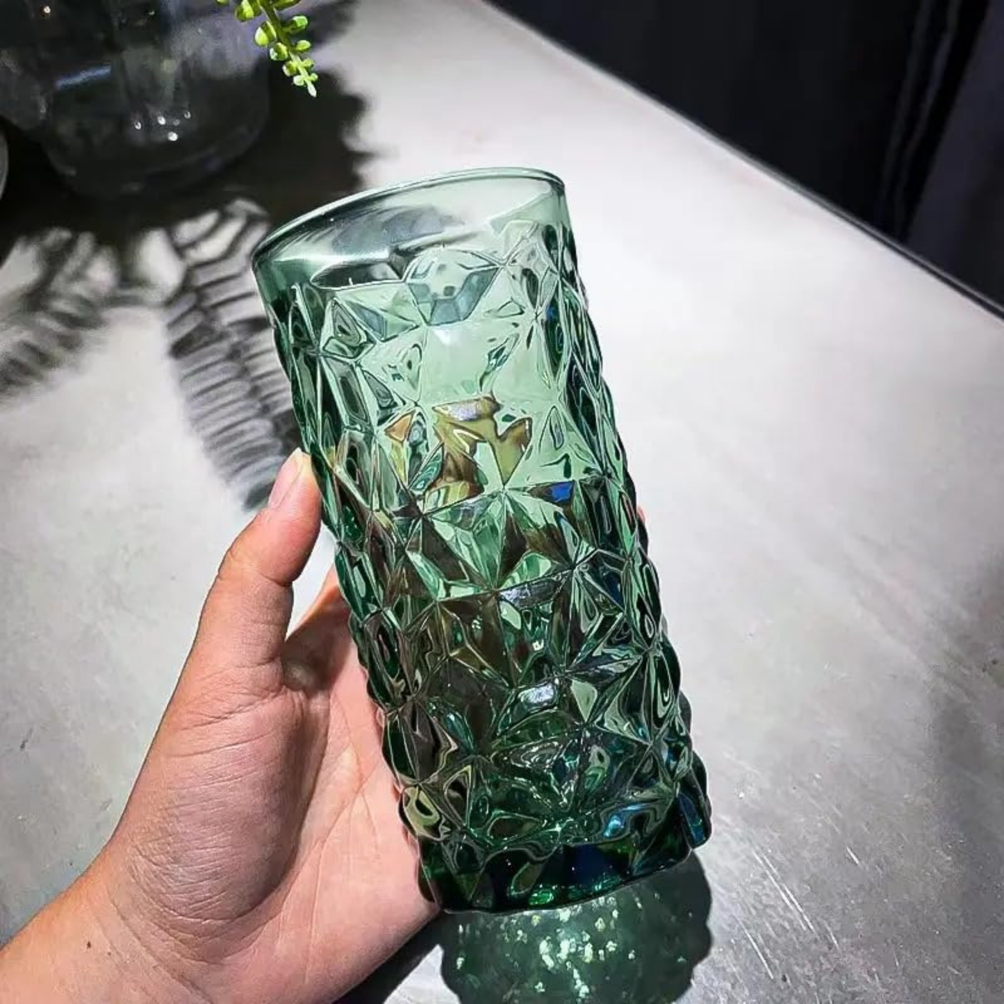 Hand holding a green patterned glass on a metallic surface