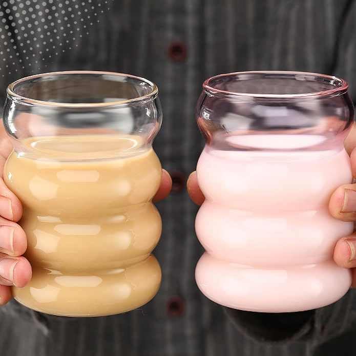 Two hands holding bubble tea cups, one with a creamy liquid and the other with a pinkish liquid.