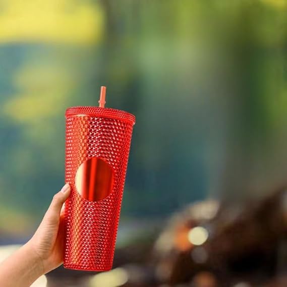 Red textured tumbler with a straw held by a hand against a blurred natural background