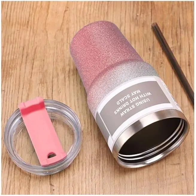 Pink glittery tumbler with straw and lid on a wooden surface