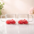 Two clear glass mugs with red flowers on a light surface.