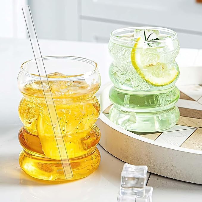 Two stacked glass tumblers with a straw and lemon slice on a light surface.