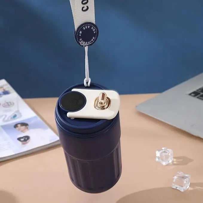 Navy blue tumbler with a white lid and black button on a desk with a magazine and laptop in the background.