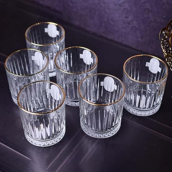 Set of six clear glass tumblers with gold rims on a dark surface.