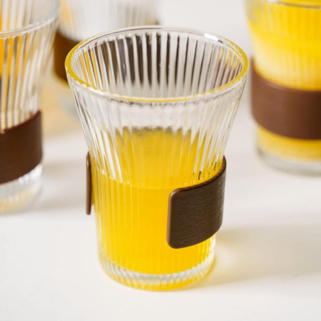 Clear glass cups with brown straps filled with a yellow liquid on a white surface.
