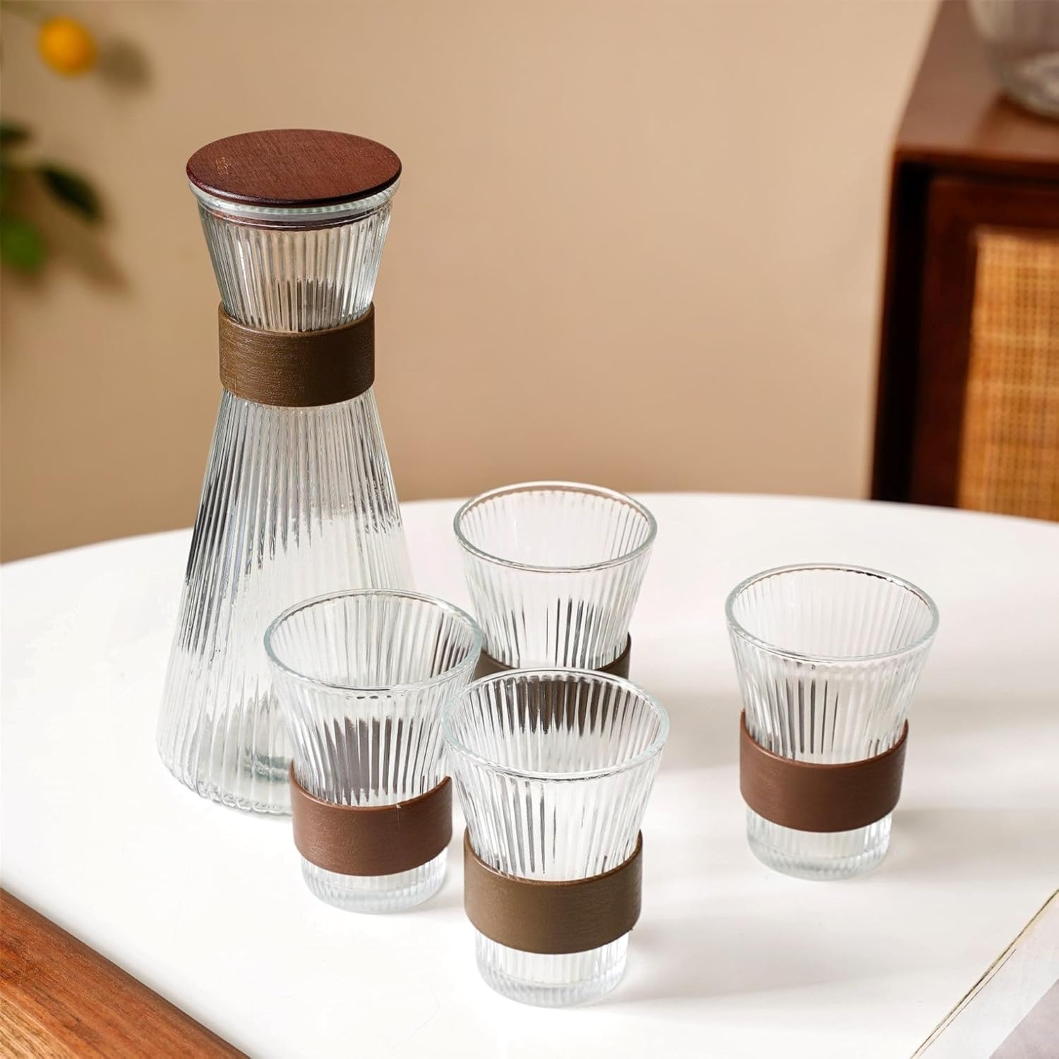 Clear glass carafe with brown lid and bands, accompanied by four matching glasses on a white surface.