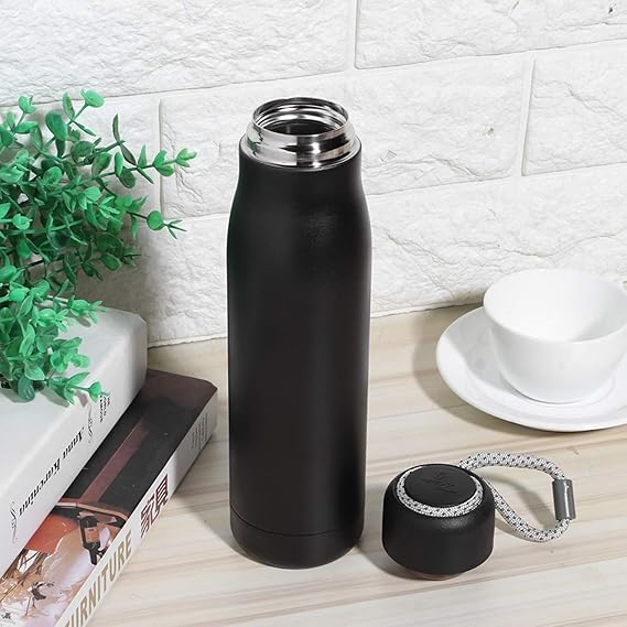 Black insulated bottle with a measuring tape on a wooden surface with a white textured wall background.