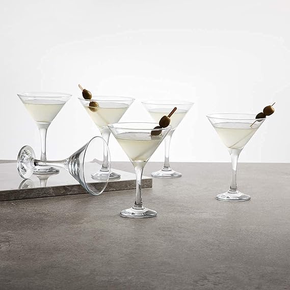 Five martini glasses with olive garnishes on a gray surface.