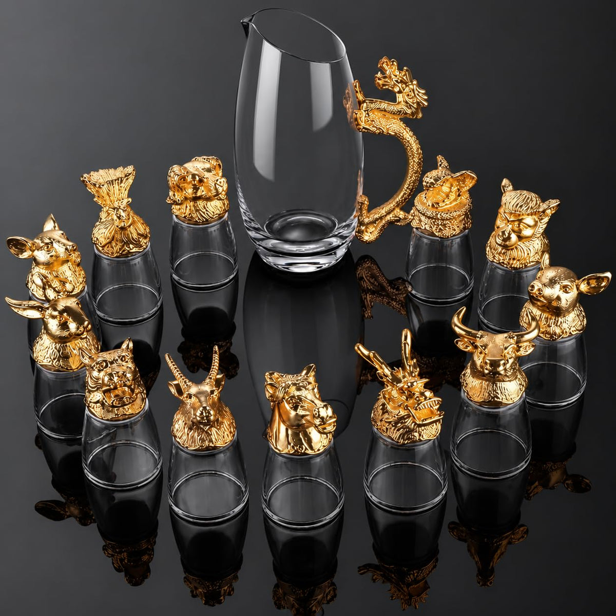 A set of clear glass shot glasses with ornate gold animal and dragon-shaped metal caps, arranged around a tall clear glass pitcher on a glossy black reflective surface.