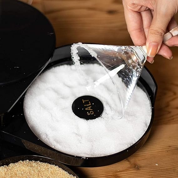 Person pouring salt into a black container with a brand logo on a wooden surface