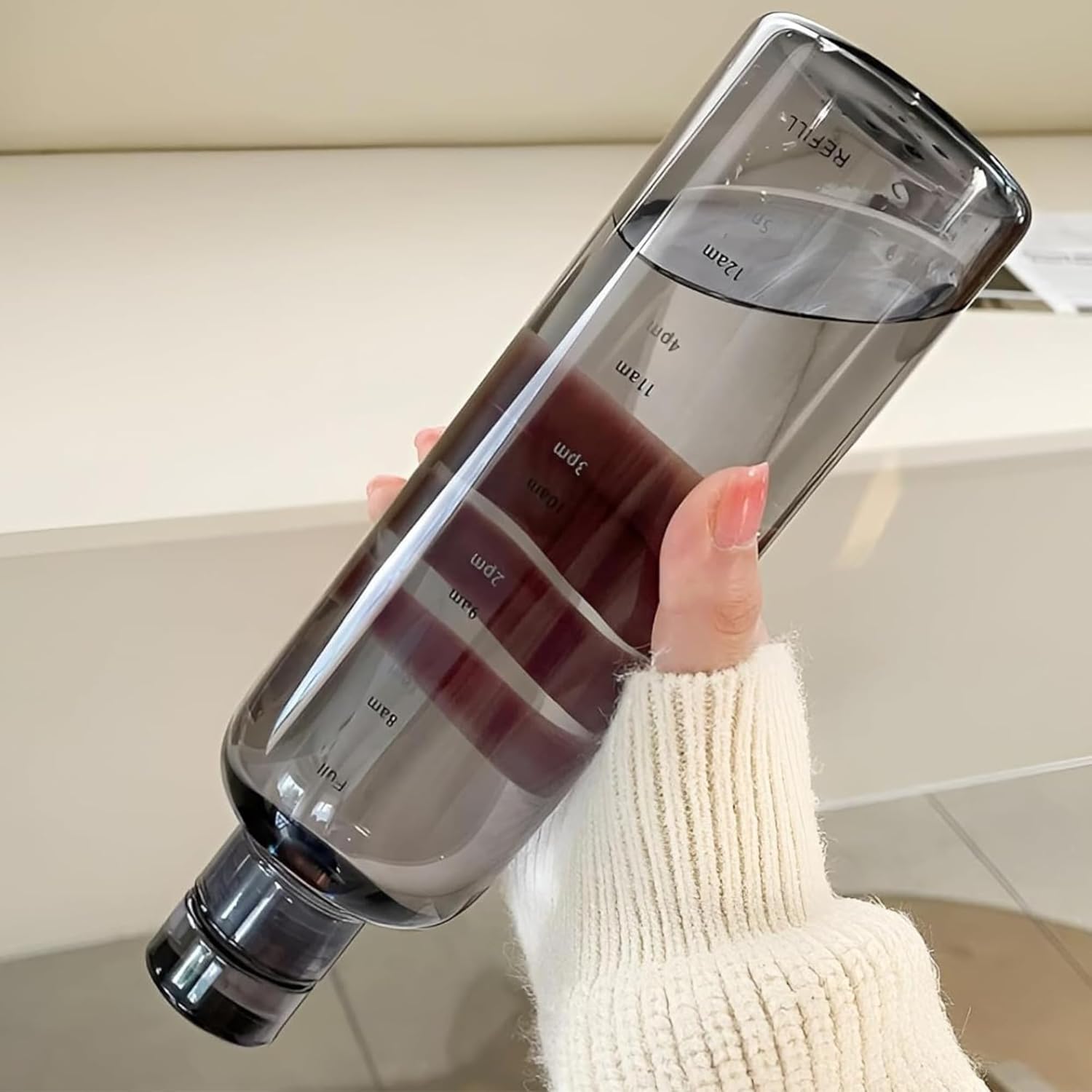 Hand holding a clear water bottle with measurement markings against a neutral background