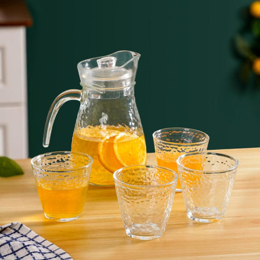 Clear glass pitcher and four glasses filled with orange juice on a wooden table.
