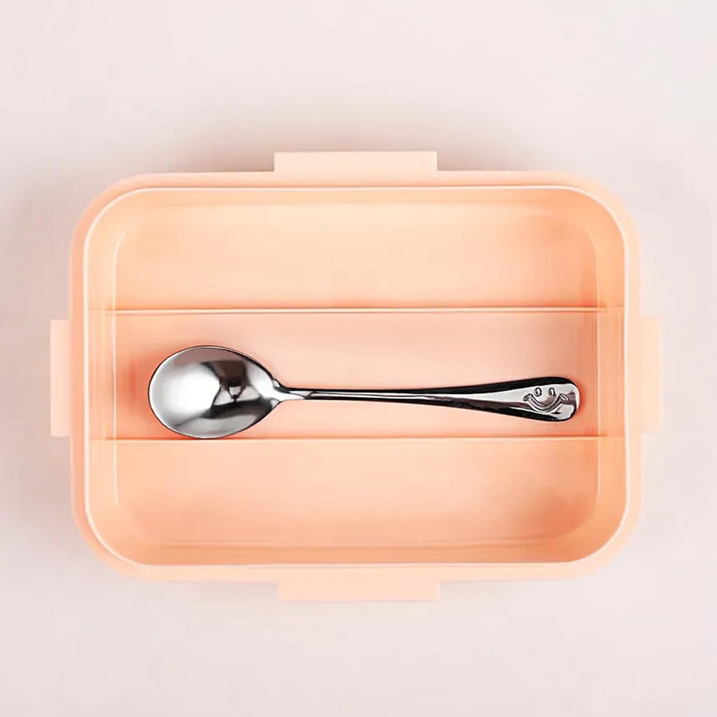 Spoon inside a peach-colored rectangular container on a light pink background