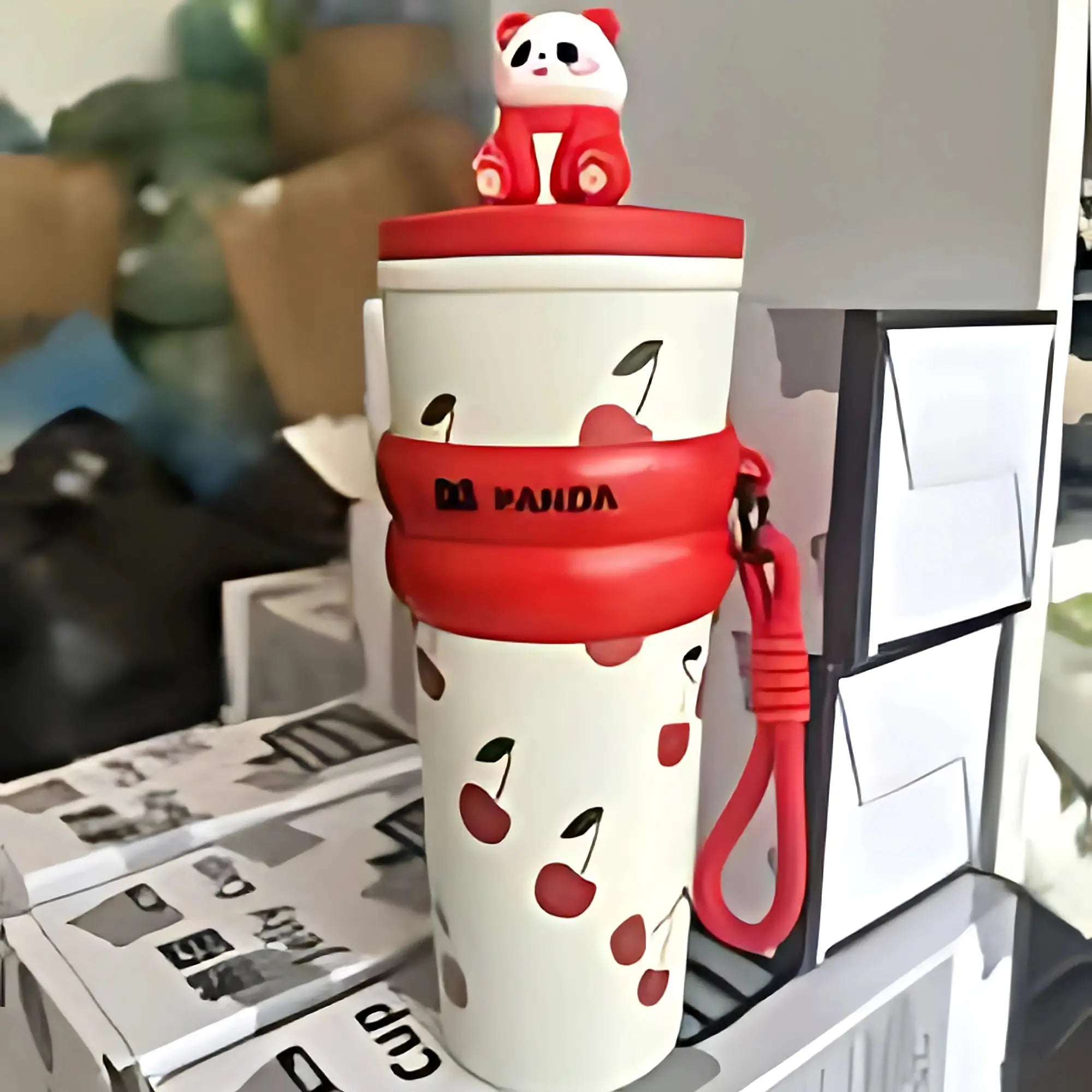 White tumbler with red accents and cherry design, featuring a panda character on top, in an indoor setting.